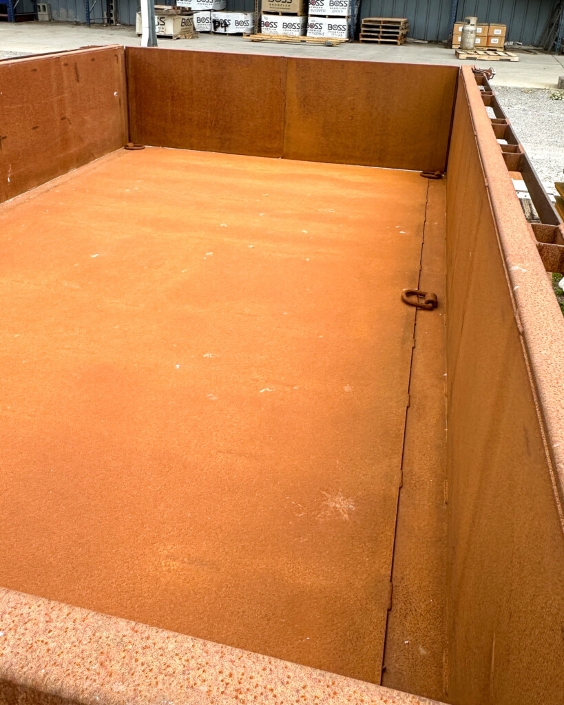 Top-down angle showing the unpainted steel bed of the MSA dump trailer, ready for customization.