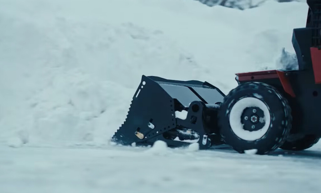 BOSS SR MAG fitted with heavy-duty bucket attachment stacking snow in a parking lot.